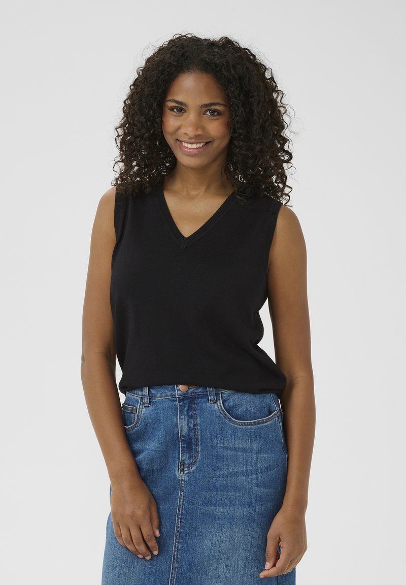 Top noir sans manches en tissu tricoté doux, associé à une jupe en denim bleue taille haute avec un bouton sur le devant et des poches.