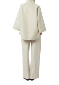 Pullover oversize color crema con colletto alto e maniche ampie, realizzato in tessuto morbido. Abbinato a pantaloni beige a gamba larga.