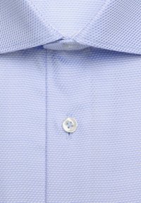Chemise habillée bleu clair avec un motif texturé, boutons blancs fermés, col classique pointu visible.
