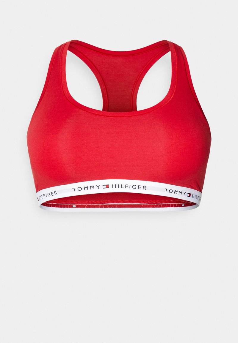 Soutien-gorge de sport rouge avec un col en U et un dos nageur. Il possède une bande élastique marquée en blanc avec du texte noir, fabriquée à partir d'un tissu lisse.