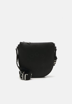 Schwarze, runde Crossbody-Tasche aus strukturiertem Material, mit einem Reißverschluss und einem Tragegurt mit kontrastierender weißer Beschriftung.