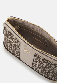 Pochette DKNY à motifs marron avec zipper doré, présentant un panneau d'accent beige et une étiquette de logo. L'intérieur est doublé d'un tissu lisse.