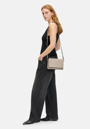 Sac bandoulière en cuir beige clair avec une texture lisse, de forme rectangulaire et une bandoulière amovible. Modèle portant un débardeur noir et un jean.