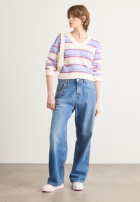 Gebreide trui met een v-hals, voorzien van roze en blauwe "tommy jeans" tekst. Gecombineerd met losse, lichtblauwe denim en lichtgekleurde schoenen.