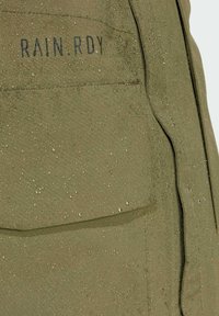 Vodootporna maslinasto zelena tkanina sa glatkom teksturom, koja ima vidljivu džep i kapljice na površini. Prikazano "RAIN.RDY" brendiranje.
