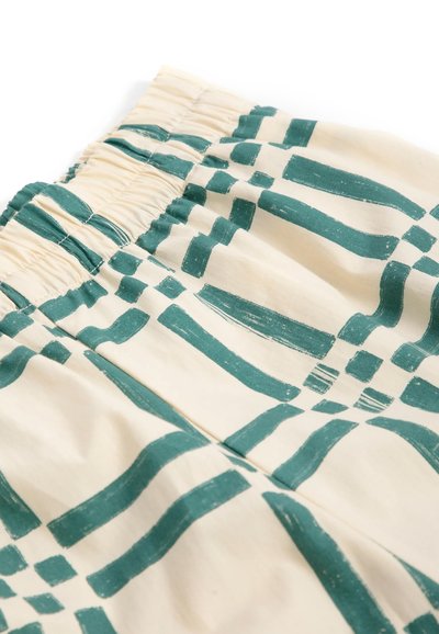 Tissu crème avec taille élastique présentant des motifs géométriques bleu sarcelle en traits verticaux et horizontaux.