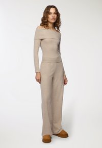 Beżowy, prążkowany zestaw dzianinowy z odkrytymi ramionami i spodniami szerokimi w nogawkach. Miękka tekstura, dopasowana góra i luźne, zwiewne nogawki.