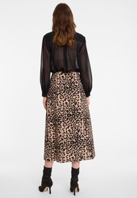 Frau, die eine durchsichtige schwarze Bluse, einen beige und schwarzen Leopardenmuster-Midirock und schwarze hochhackige Stiefeletten trägt, von hinten betrachtet.