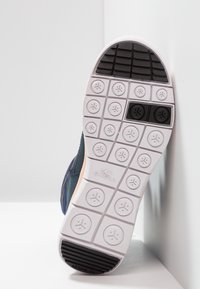 Parte superior del zapato hecha de textil azul marino con un acabado suave. La suela blanca presenta un agarre texturizado y patrones circulares, con la marca en el talón.
