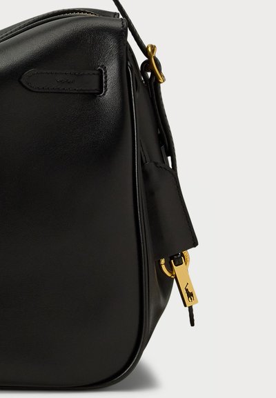 Juodas odinis rankinės su lygiu paviršiumi, apvalia forma, auksinėmis detalėmis ir užtrauktuku su pakabuku.