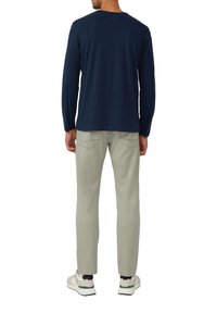 Langärmliges, dunkelblaues Hemd mit Rundhalsausschnitt, kombiniert mit hellgrauen Hosen und weißen Sneakers. Das Outfit hat einen lässigen Schnitt mit minimalen Details.