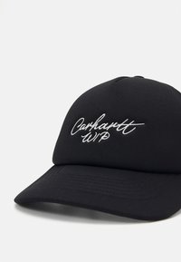 Gorra negra con visera curva, con el texto bordado en blanco "Carhartt WIP" en la parte frontal. La tela tiene una textura suave con detalles de costura.