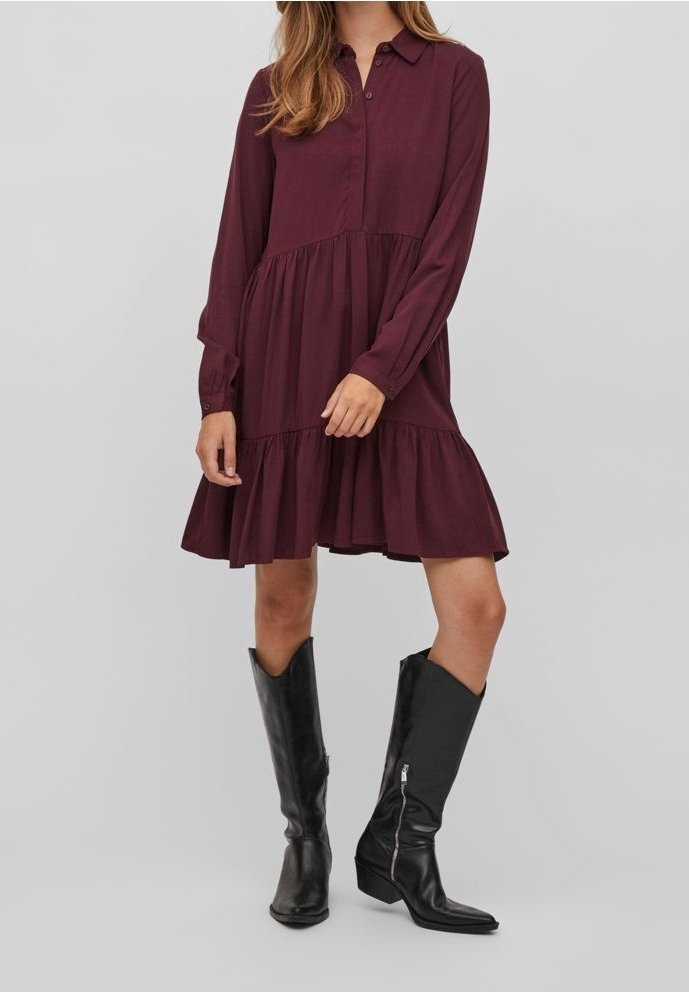 Abito lungo bordeaux a maniche lunghe con colletto a camicia, design a strati e orlo arricciato. Abbinato a stivali neri di pelle al ginocchio.