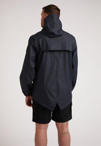 Veste imperméable bleu marine avec un col haut, une capuche ajustable et des poignets élastiques, présentant un ourlet arrière plus long et une texture lisse.
