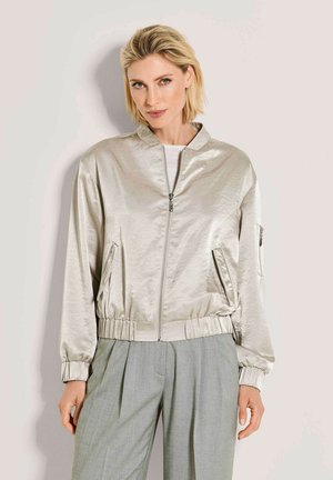 Metallic silberne Bomberjacke mit elastischen Bündchen und Bund, vorderem Reißverschluss und Seitentaschen; getragen über einem weißen, strukturierten Oberteil und grauer Hose.