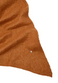Miękka, frotte tekstura koca w kolorze pomarańczowo-brązowym, z zaokrąglonym brzegiem i małym metalowym logo na powierzchni.