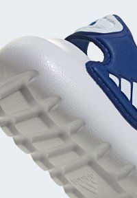 Niebieski sportowy but z białymi akcentami, posiadający teksturowaną gumową podeszwę i gładką cholewkę. Zawiera charakterystyczny pasek i otwory wentylacyjne.