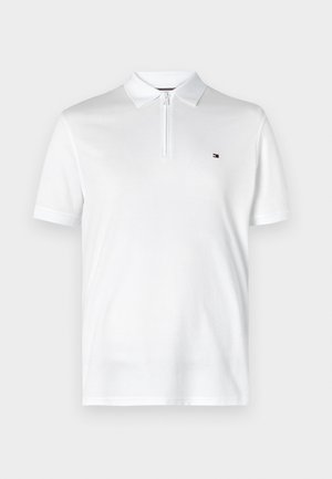 Fehér pólóing sima anyagból, zipzáros gallérral és rövid ujjakkal. Kis logófolt a bal mellrészen.