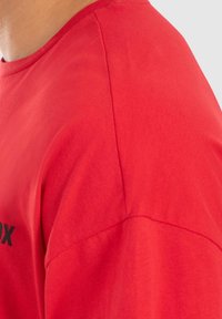 Rød bomulds T-shirt med rund hals, korte ærmer og en glat tekstur; prydet med sort tekst nær kanten.