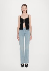 Black cropped top with spaghettis straps, featuring a hook closure and silver studs. Paired with light blue flared jeans and black heels.