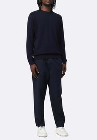 Maglione blu navy con collo rotondo e maniche lunghe, abbinato a pantaloni blu navy larghi e sneaker bianche. Texture liscia, design minimal.