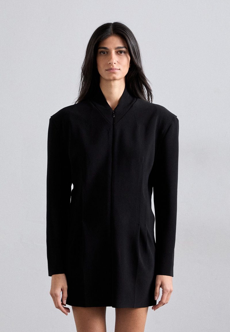 Black tailored coat dress with a high collar, structured shoulders, vertical seam details, and side pockets. Made from a smooth fabric.