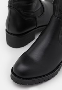 Botas de hombre de cuero negro, con punta redondeada, superficie texturizada y suela de goma gruesa y con relieve. Presentan costuras a lo largo del borde.