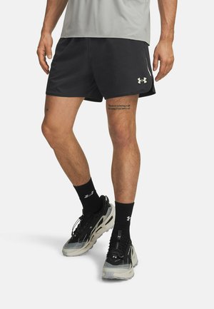 Schwarze sportliche Shorts mit glatter Textur, akzentuiert durch ein reflektierendes Logo. Getragen mit schwarzen Sportsocken und grauen Turnschuhen.