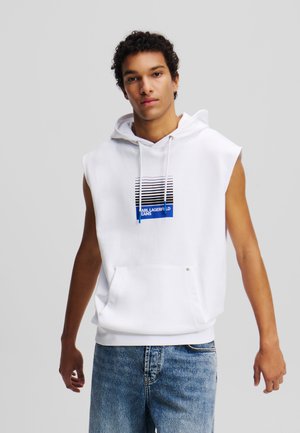 Witte mouwloze capuchontrui met een voorzak. Heeft een grafisch ontwerp met horizontale strepen en blauwe accenten. Casual fit.