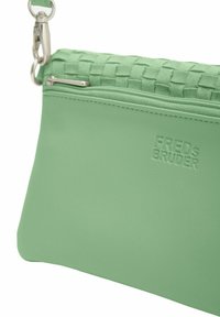 Borsetta in pelle verde con una parte superiore tessuta, chiusura a zip e una clip in metallo per il fissaggio. Presenta il logo del marchio impresso sulla parte frontale.