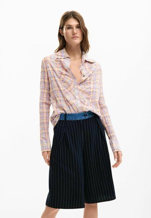 Ruuduline hele-roosa ja sinine pluus volangidega kaelusega; koos tumesiniste triibuliste lühikpükstega, millel on teksariidest vöökoht.