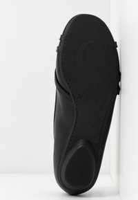 Chaussure noire à bout fermé anglée pour montrer la semelle texturée avec des motifs circulaires et le marquage taille 37 sur fond blanc.