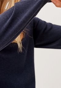 Granatowy sweter dzianinowy z długimi rękawami. Tkanina wydaje się mi�ękka i strukturalna, prezentując swobodny krój i minimalne detale.