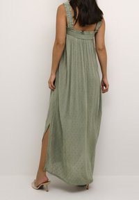 Robes maxi longues vertes avec un motif texturé, bretelles froncées et fentes latérales pour une plus grande liberté de mouvement ; fabriquées dans un tissu léger.