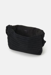 Sac en crochet noir avec un extérieur texturé et tissé et un intérieur en tissu noir lisse. Présente un design simple et ouvert, avec une anse douce.