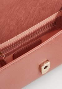 Rosa texturerad läderväska med insida, zipfack, slät foder och ett kvadratiskt lås i guldfärg.