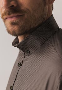 Bruin overhemd met patroon en kraag, voorzien van een gestructureerd ontwerp, knoopsluitingen en een textuurstof met een subtiel geometrisch patroon.