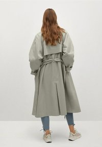 Lys grå trenchcoat med bælte i livet, brede ærmer og rygslids. Stylet med blå jeans og hvide sneakers. Glat tekstur.