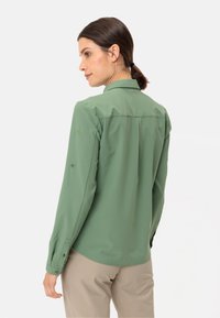 Camicia a maniche lunghe verde chiaro con colletto, polsini con bottoni e un logo sottile ricamato sulla manica. Tessuto morbido e traspirante.