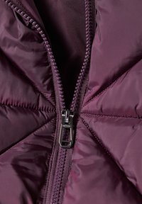 Gros plan d'une veste matelassée violet foncé avec une fermeture éclair argentée partiellement ouverte au centre.