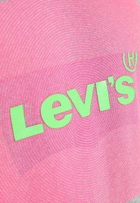 Tissu rose avec un logo "Levi's" en relief de couleur verte, accompagné d'un motif texturé circulaire en arrière-plan et d'un symbole de marque déposée.