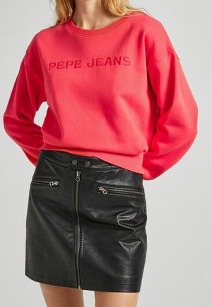 Kräftig pinkes Sweatshirt mit "PEPE JEANS" in dunklerem Pink bestickt. Kombiniert mit einem eng anliegenden schwarzen Rock aus Kunstleder mit Reißverschlusstaschen.