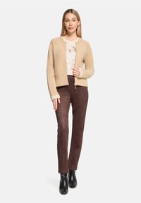 Pull beige et duveteux à encolure ronde, associé à un pantalon slim marron foncé. Des bottines noires complètent la tenue.