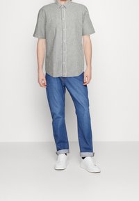 Kurzärmliges gestreiftes Hemd in Grau und Weiß, mit Knopfleiste, kombiniert mit hellblauen Jeans und weißen Sneakern, vor einem schlichten Hintergrund stehend.