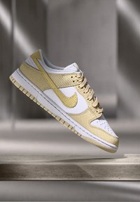 Tenisky Nike Dunk majú béžový kordové zvršok s bielymi koženými akcentmi, okrúlu špičku, gumovú podrážku a tonálne šitie na boku.
