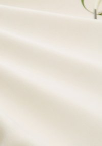 Cremefarbener Stoff mit einer glatten, leicht strukturierten Oberfläche, der sanfte Falten und subtile Lichtreflexionen aufweist.