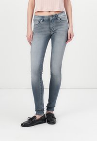 Jeans ajustados de mezclilla de un azul deslavado, con una cinta media, diseño de cinco bolsillos y costuras simples. Combinados con zapatos planos negros.