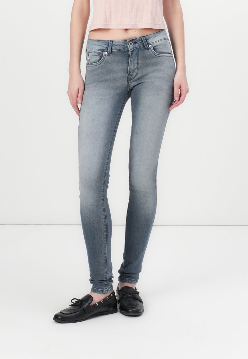 Jeans ajustados de mezclilla de un azul deslavado, con una cinta media, diseño de cinco bolsillos y costuras simples. Combinados con zapatos planos negros.