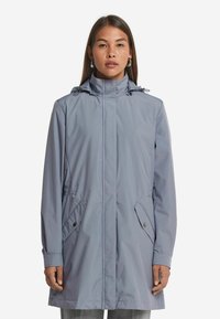 Ljusgrå vattentät jacka med hög krage, dragsko i huvan och två sidofickor, med en slät textur och modern design.