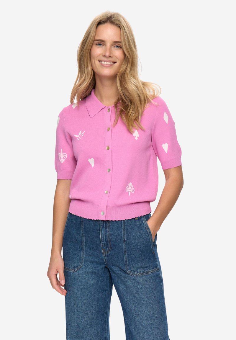 Roze kort mouwtje vestje met een geschulpte zoom en lichtgewicht gebreide stof. Heeft witte geborduurde motieven: harten, schoppen en abstracte ontwerpen.